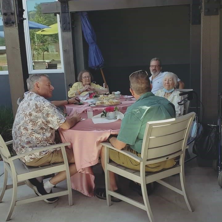 A group of people sitting around a table outdoors, engaged in conversation.