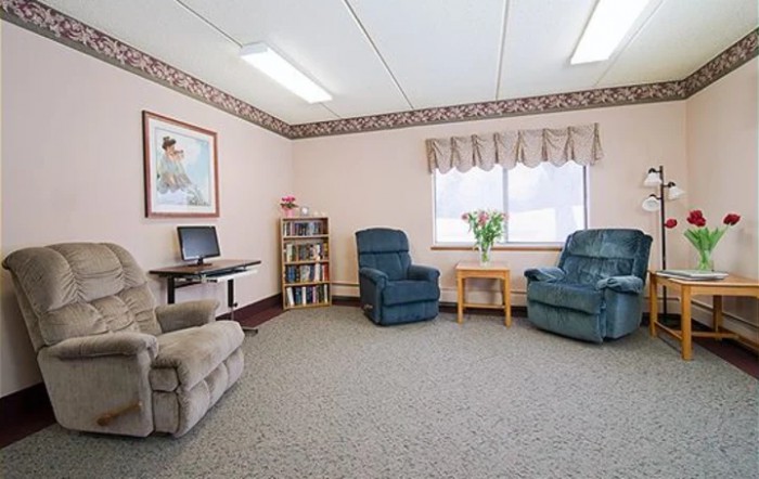 A cozy living room with recliner chairs, a small table with flowers, and a computer desk.