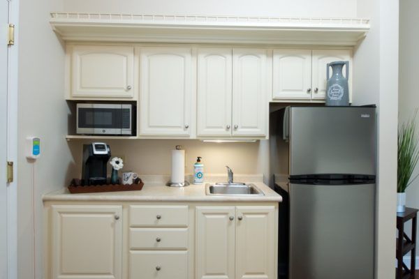 A compact kitchen featuring cabinets, a microwave, coffee maker, sink, and refrigerator.