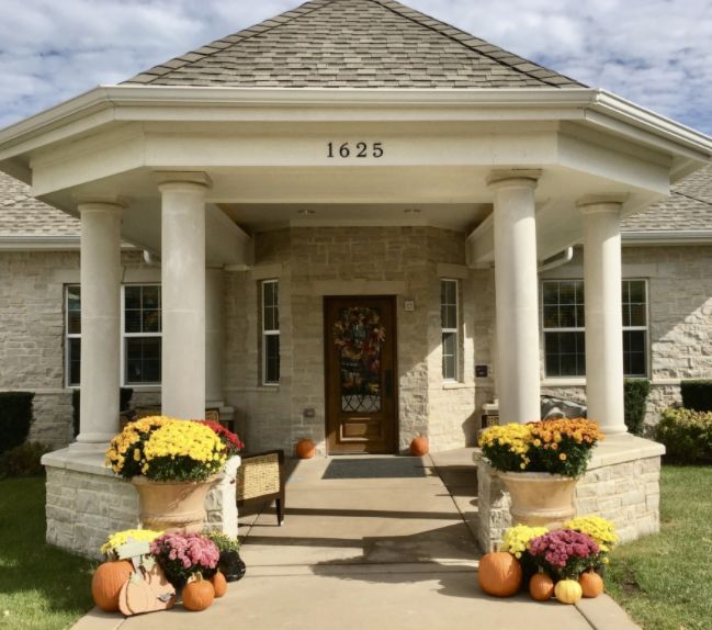 A welcoming porch decorated with flowers and pumpkins, showcasing a lovely stone house facade.