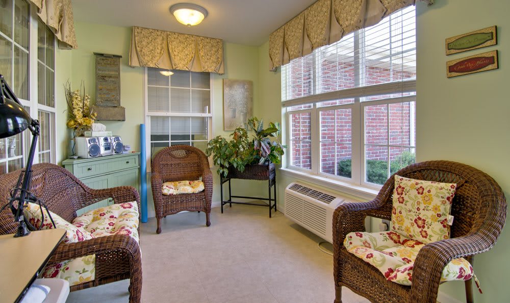 A cozy indoor living area with wicker chairs, large windows, and vibrant plants.
