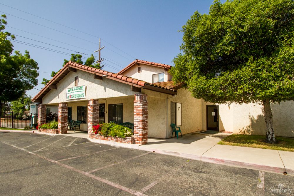 A small clinic with a tiled roof and stone columns, surrounded by trees and a parking lot.