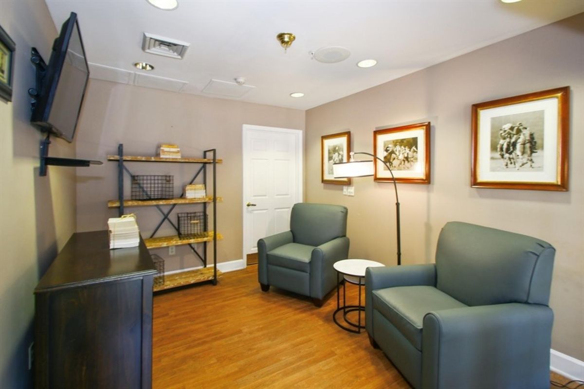 A cozy waiting room featuring comfortable armchairs, a shelving unit, and framed artwork on the walls.