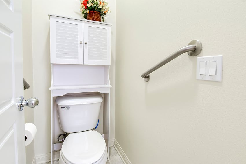A bathroom featuring a toilet with an over-the-toilet cabinet and a safety handrail.