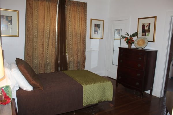 A cozy bedroom with a neatly made bed, brown curtains, and a wooden dresser.