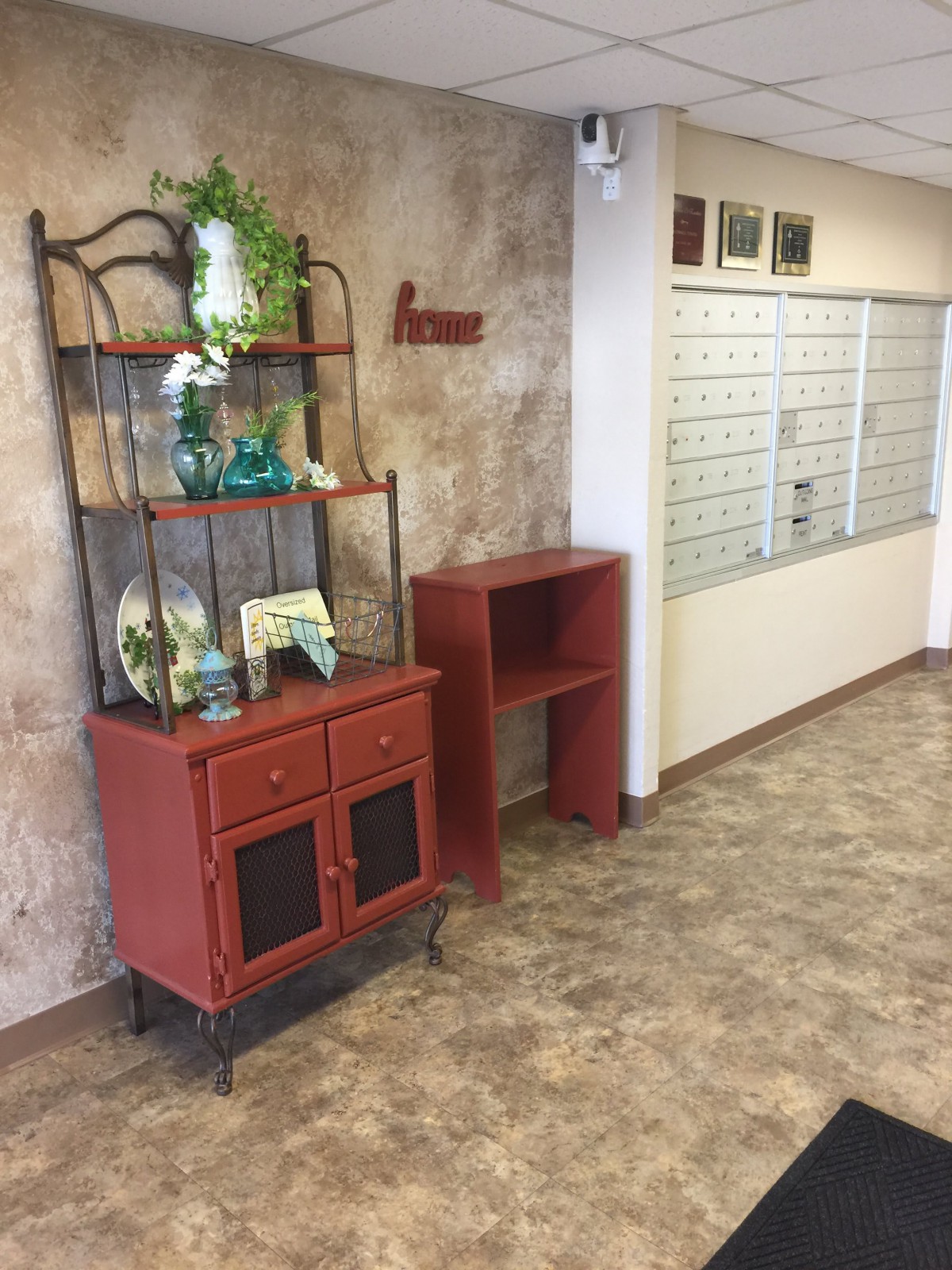 A decorated office corner with a red shelf and potted plant.