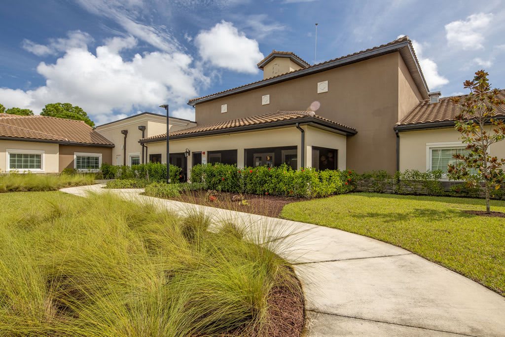 A modern building with a winding pathway surrounded by lush greenery under a cloudy sky.