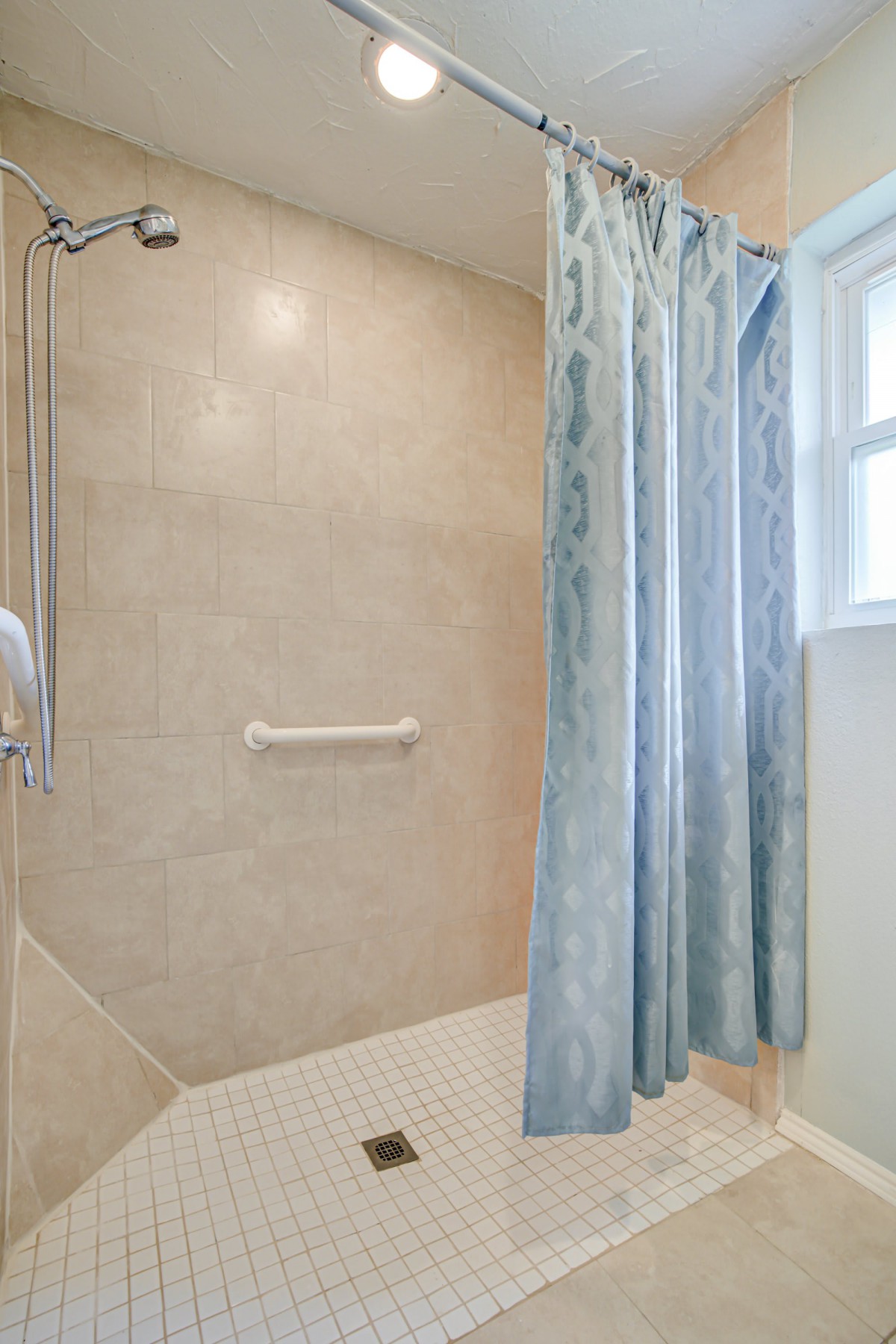 A bathroom shower area with a blue patterned curtain and a grab bar.