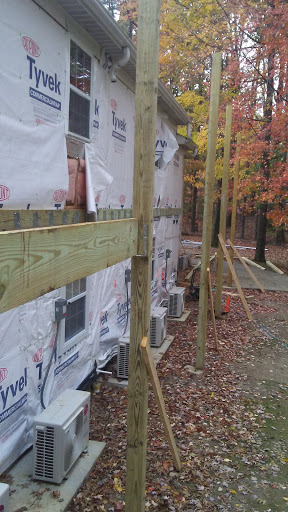 Construction site showing wooden supports and exterior walls covered in protective sheeting, surrounded by autumn foliage.