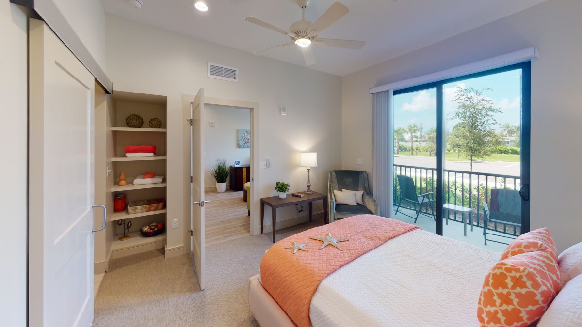 A modern bedroom with a cozy bed, stylish decor, and large windows leading to a balcony.