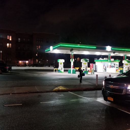 A nighttime view of a gas station with illuminated signage and a parked car.