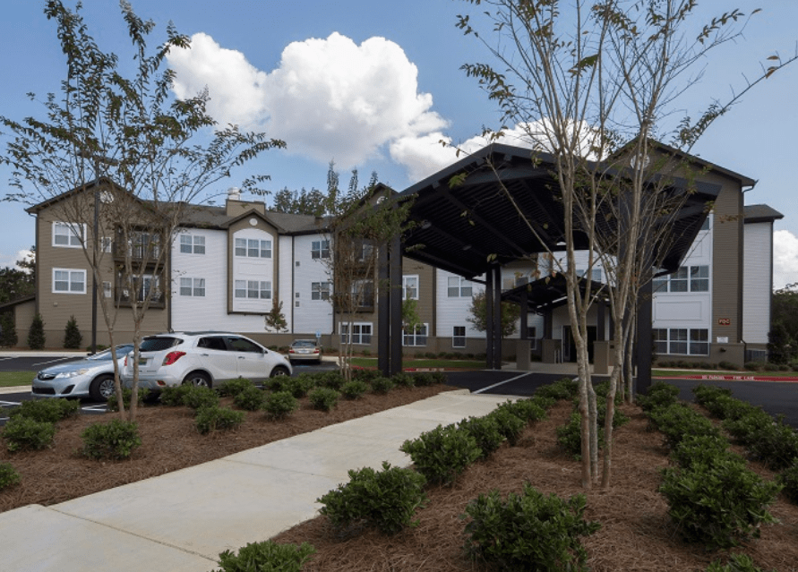 A modern building with a covered entrance, surrounded by trees and landscaping.
