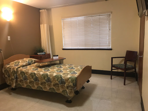 A simple and cozy bedroom featuring a bed with floral bedding, a window with blinds, and a wooden chair.