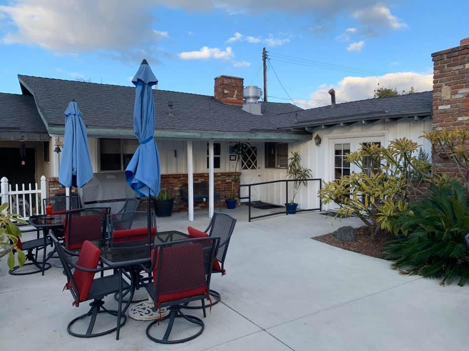 A cozy outdoor patio area with tables, chairs, and umbrellas against a building backdrop under a partly cloudy sky.