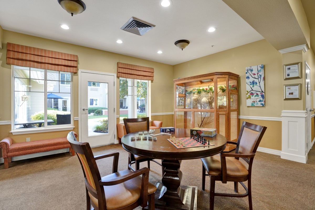 A cozy interior room featuring a round table and chairs, surrounded by windows and a display cabinet.
