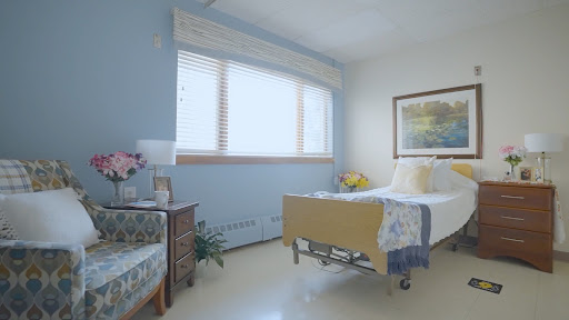 A bright and serene hospital patient room featuring a bed, a comfortable chair, and natural light streaming in through the window.