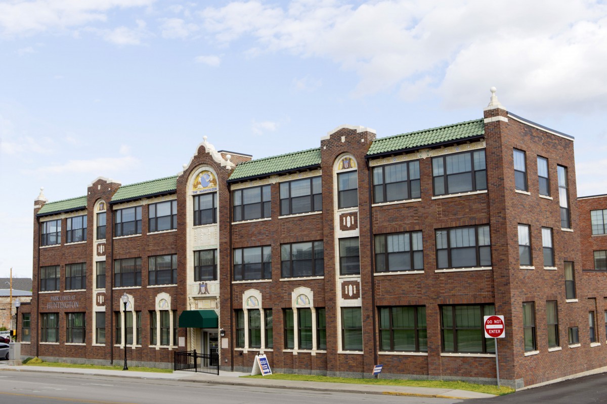 A three-story brick building with large windows on a city street under a cloudy sky.