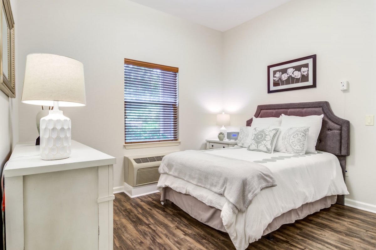 A cozy bedroom with a neatly made bed, nightstand, and soft lighting.