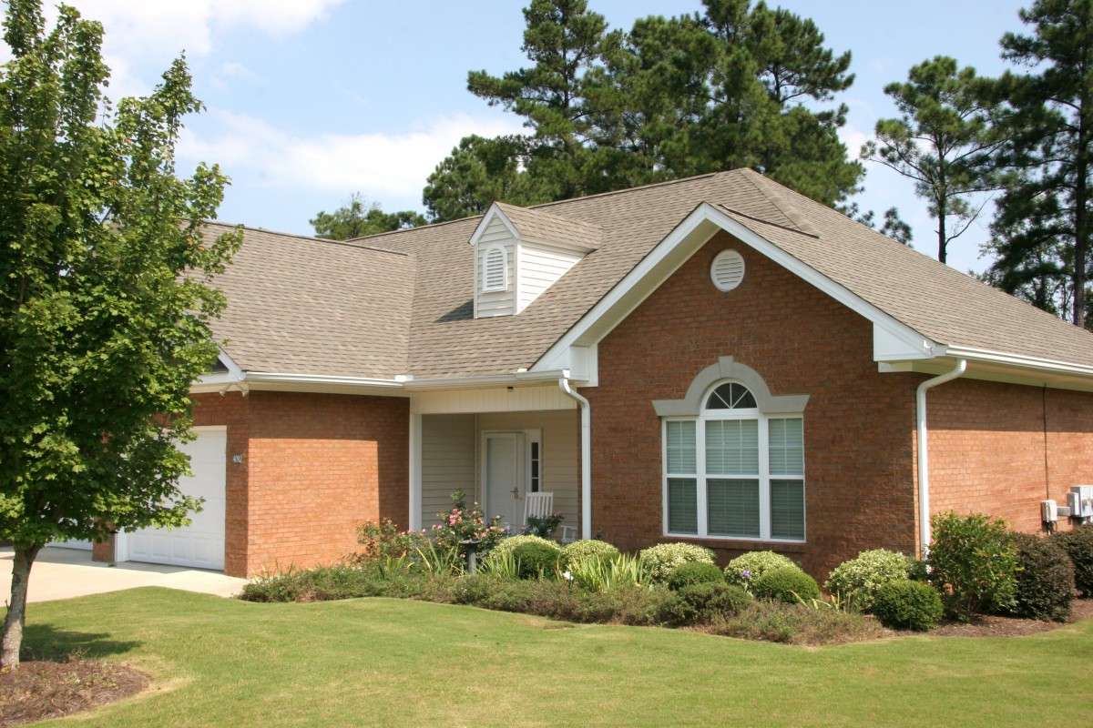 A suburban brick house with a well-maintained lawn and surrounding trees.