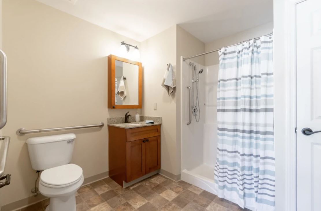 A clean and modern bathroom featuring a toilet, sink with mirror, and a shower with a striped curtain.
