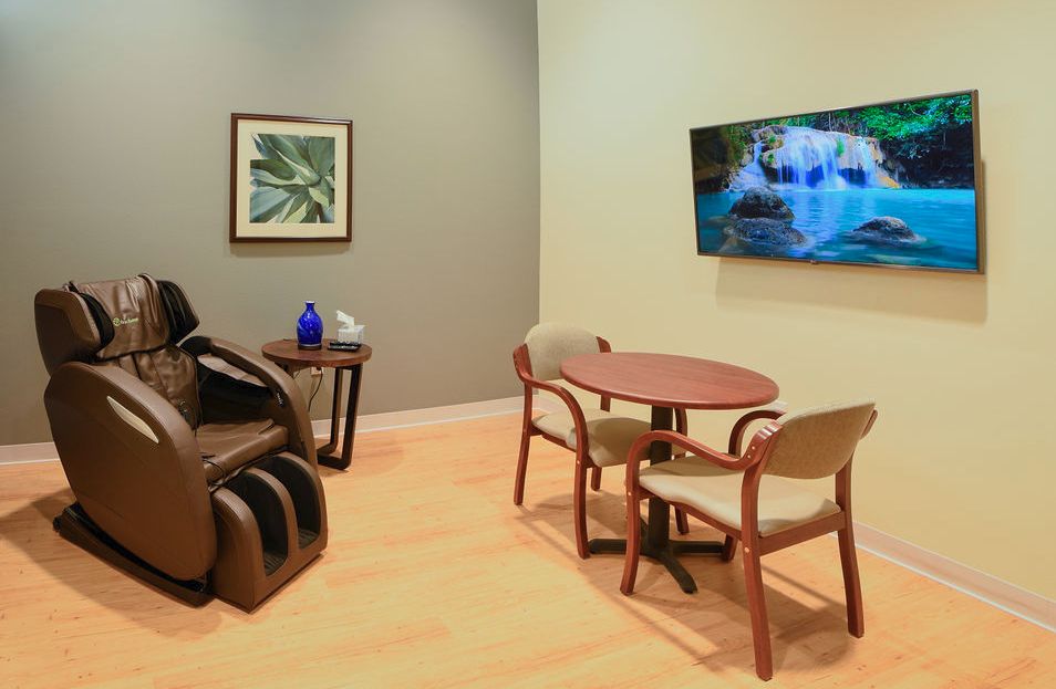 Relaxing waiting room with a massage chair, table, and television.
