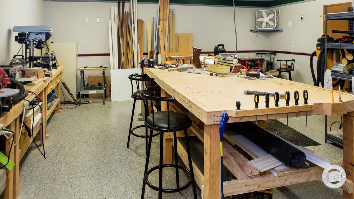 A woodworking workshop featuring a wooden workbench with tools and stools around it.