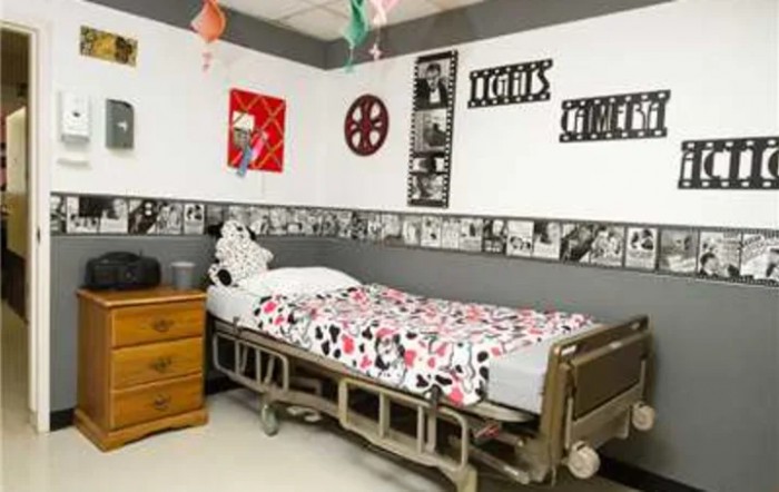 A movie-themed bedroom with a hospital bed, decorated with film reel posters and a dresser.