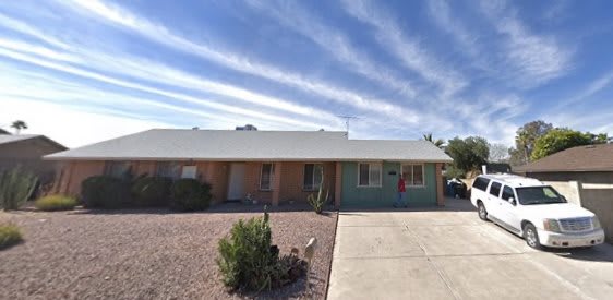 A single-story house with a xeriscaped front yard under a blue sky with streaked clouds.