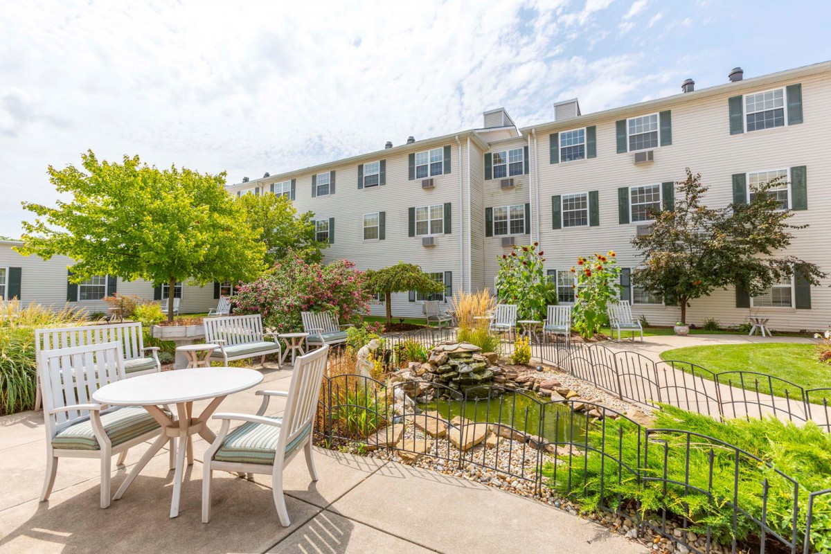 A sunny courtyard with patio furniture, landscaping, and a multi-story building in the background.