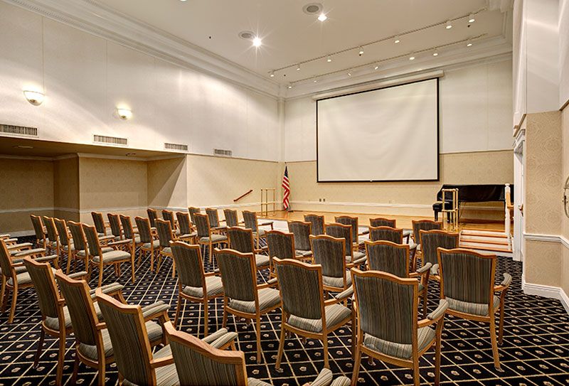 An empty conference room with rows of chairs facing a large projector screen.