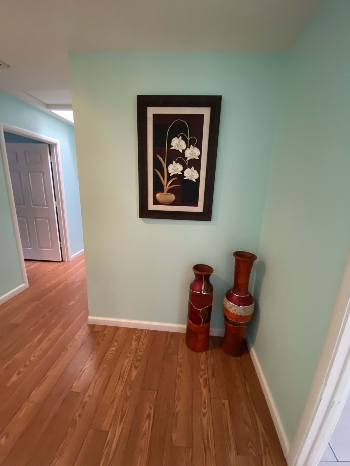 A hallway with a floral painting and two decorative vases on a wooden floor.