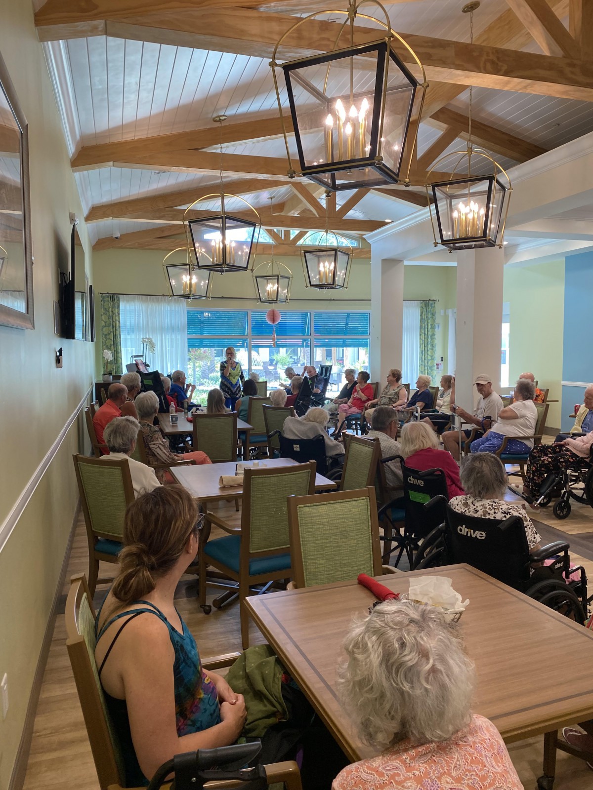 A community gathering indoors with people seated at tables and chairs.
