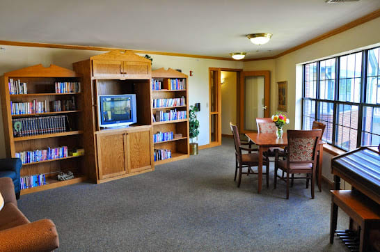 A cozy living room with a television, bookshelf, and a table with chairs.