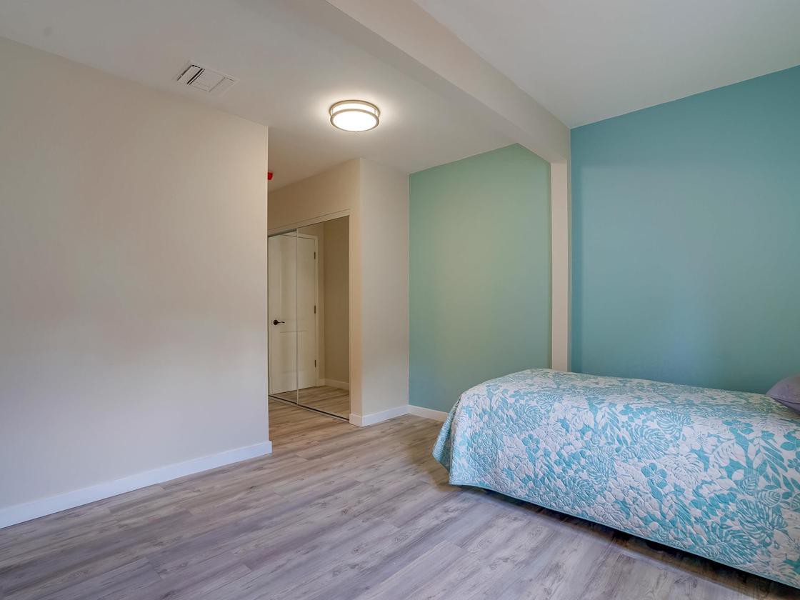 A minimalist bedroom with light wood flooring and a blue accent wall.