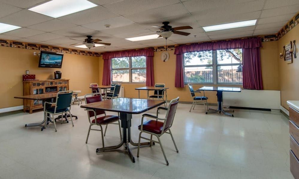 An empty dining area with tables and chairs, featuring large windows and ceiling fans.