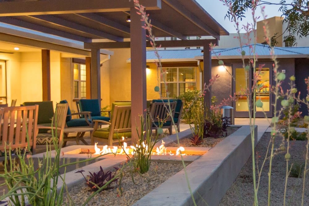 A cozy outdoor patio area with a pergola and fire pit, surrounded by comfortable seating and landscaped plants.