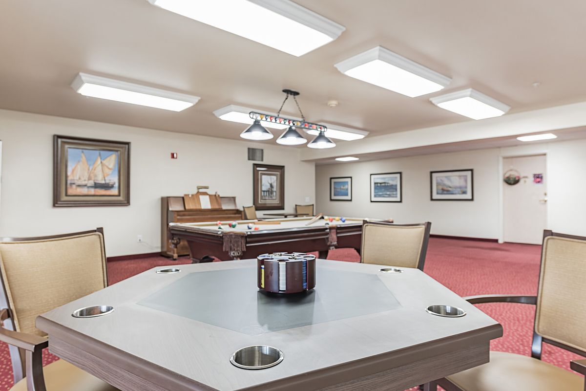 A recreation room featuring a pool table and poker table, with framed artwork and seating areas.
