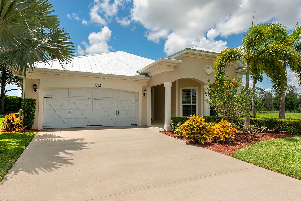 A suburban house with a large driveway and well-maintained landscaping, including palm trees under a partly cloudy sky.