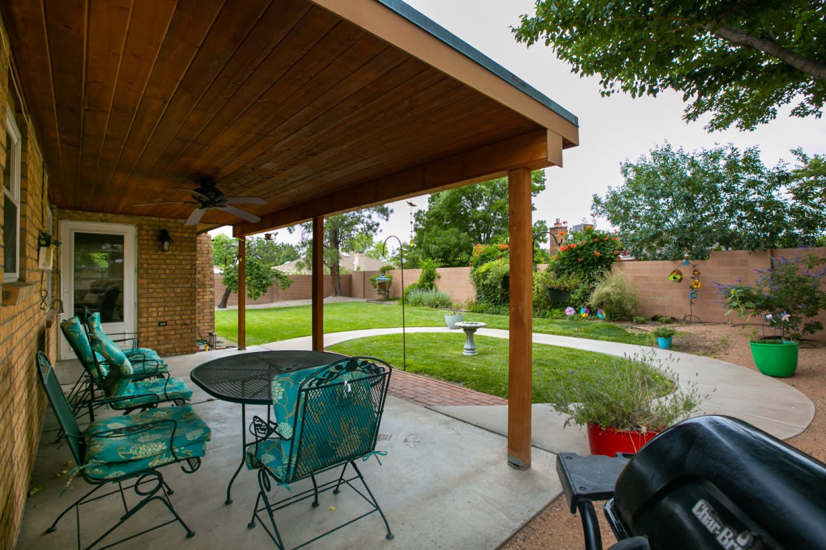 A covered patio with outdoor seating overlooks a well-maintained backyard garden.