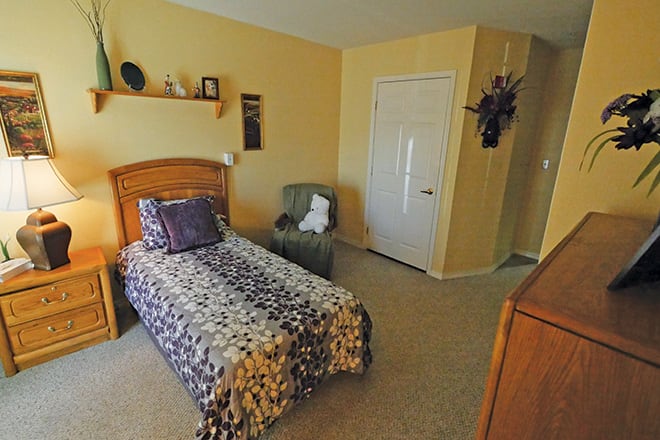 A cozy bedroom with a single bed, small shelf, and comfortable chair.