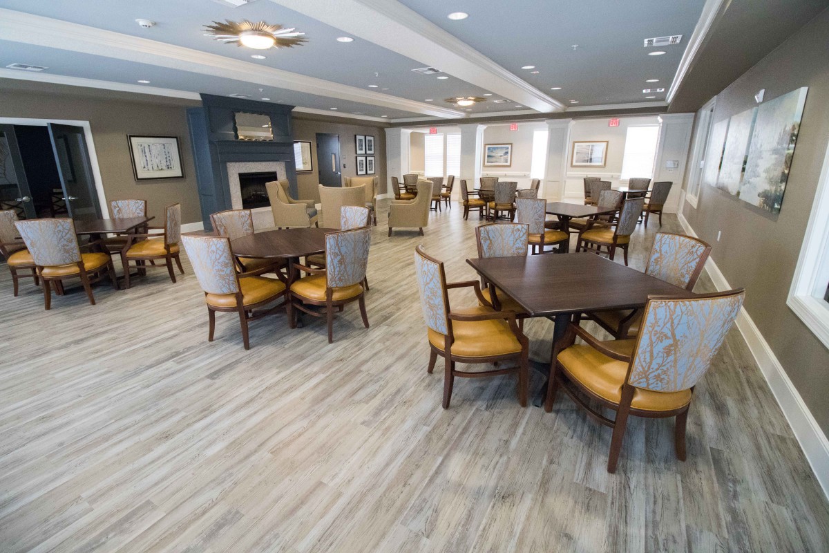 A spacious and elegantly furnished dining area with multiple tables and chairs, featuring a wooden floor and a fireplace.