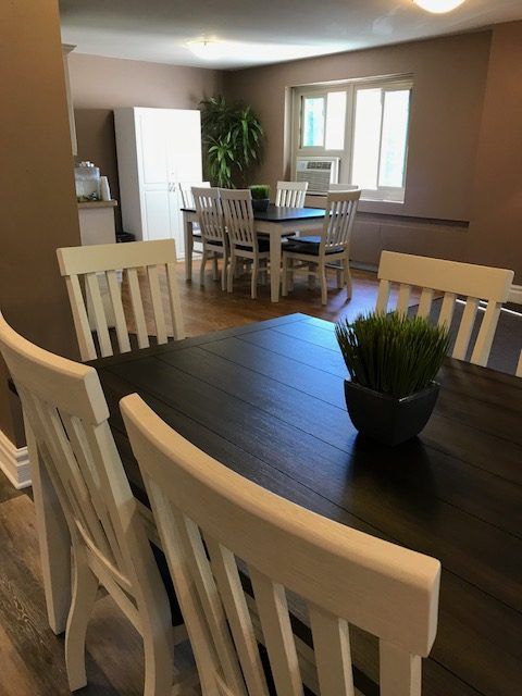 A dining area with a dark wooden table, surrounded by white chairs, and a small plant centerpiece.