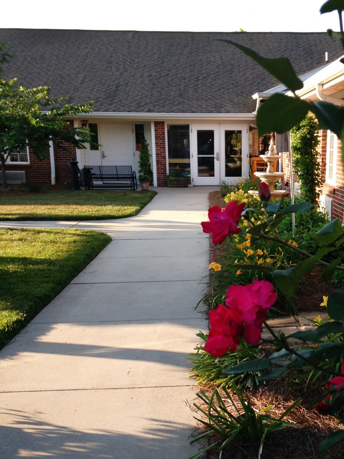 A serene garden path lined with vibrant red flowers leading to a cozy house entrance.