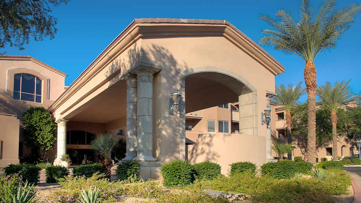 A sunny view of a large residential building with an arched entrance and manicured landscape.