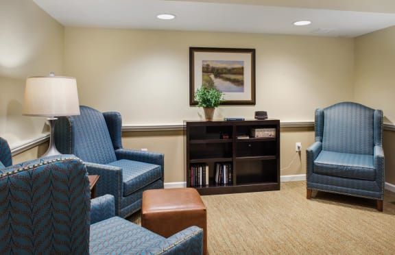 A cozy living room with blue armchairs, a bookshelf, and wall art.