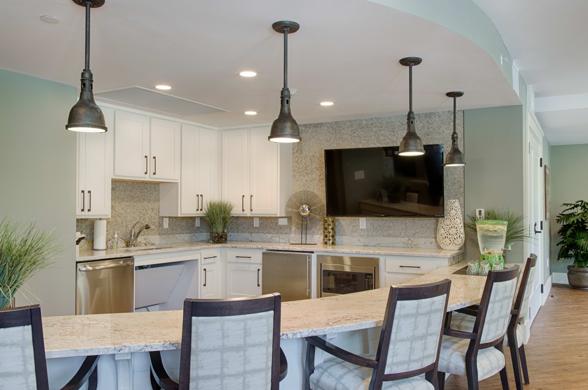 A modern kitchen interior featuring bar stools, pendant lighting, and a mounted television.