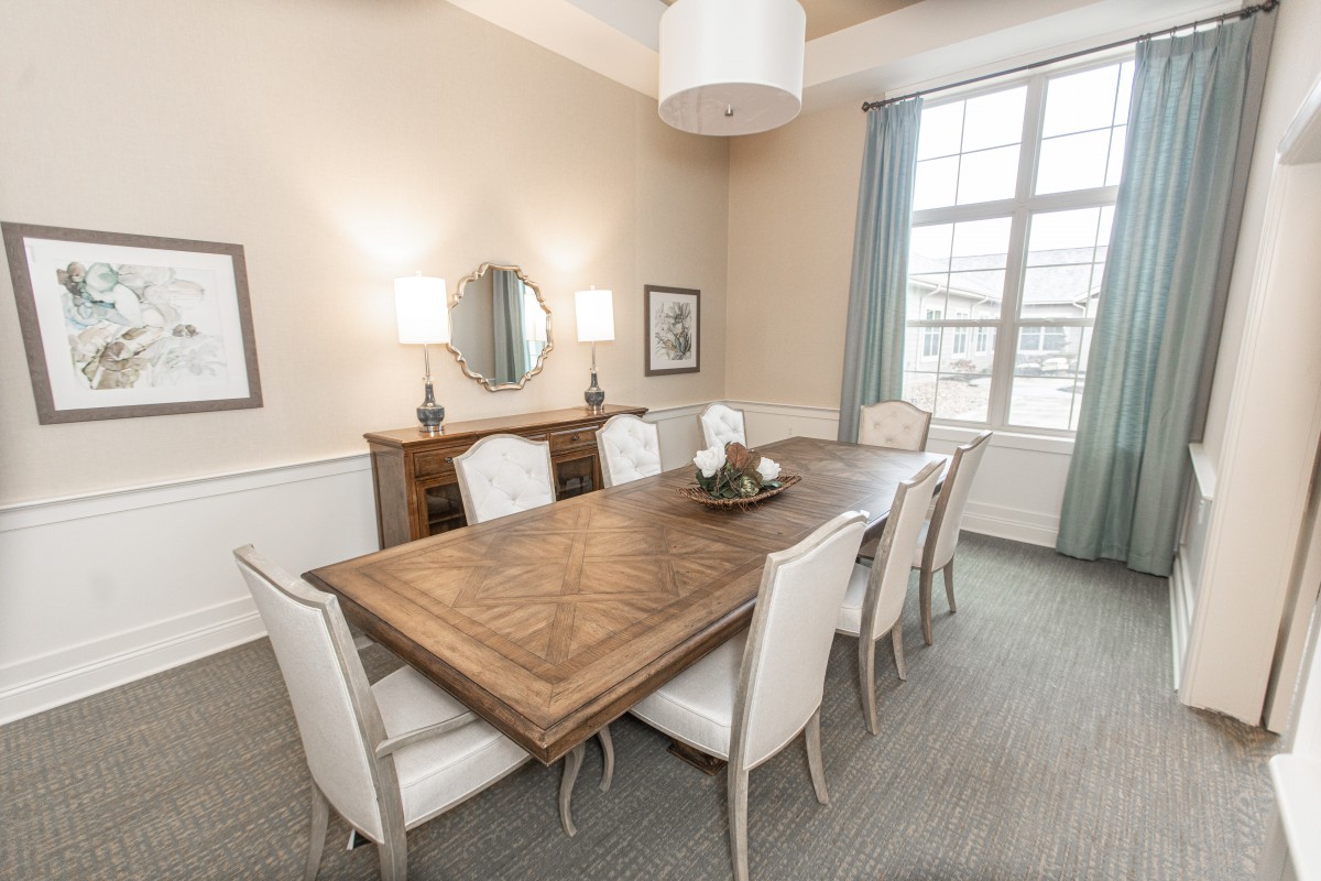 A well-decorated dining room featuring a large wooden table with white chairs, ambient lighting, and a window with curtains.