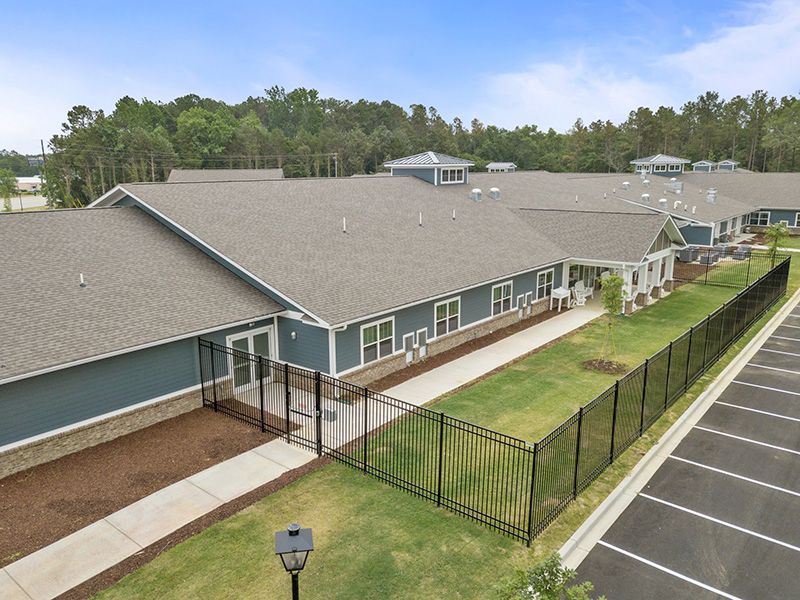 A modern building with a fenced area and parking lot, surrounded by trees.