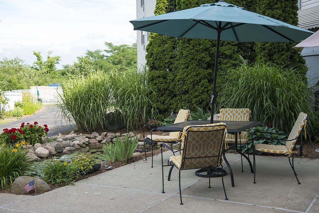 A cozy patio setup with a table, chairs, and an umbrella amidst lush garden greenery.