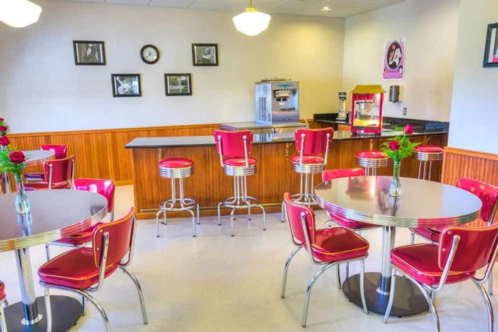 A retro-style diner interior featuring red bar stools and chairs, with vintage decor.